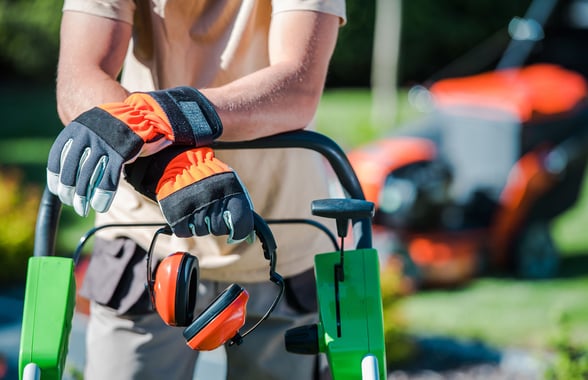 Man leaning on a lawnmower with ear protection in his hands